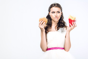 thoughtful young bride in wedding dress with burger and french fries looking up isolated on white