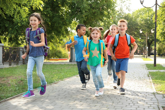 Cute little children with backpacks running outdoors. Elementary school