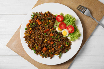 Plate with lentil porridge and fresh vegetables on wooden table, top view