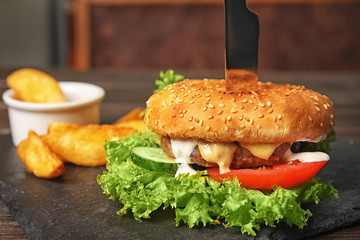 Tasty burger and fries served on slate plate, closeup