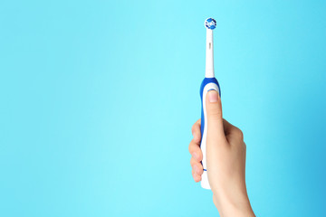 Woman holding electric toothbrush against color background