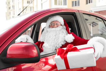 Authentic Santa Claus with gift box driving car, view from outside