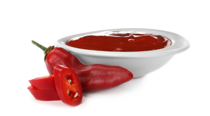 Bowl with spicy chili sauce and fresh pepper on white background