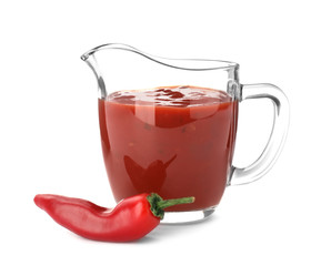 Jug with spicy chili sauce and fresh pepper on white background
