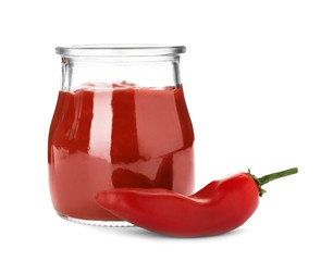 Jar with spicy chili sauce and fresh pepper on white background