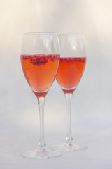 Tchin-tchin/Two glasses of champagne with raspberries on sunlight on white background, vertical picture