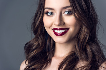 Fototapeta premium close-up portrait of attractive young woman with curly hair and stylish makeup looking at camera isolated on grey