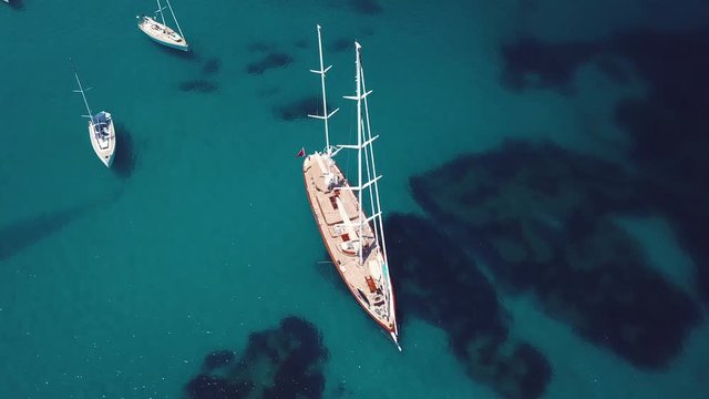 Aerial view of a beautiful sailing boat and other small boats on an emerald and transparent mediterranean sea. Gulf of the Great Pevero, Emerald Coast (Costa Smeralda), Sardinia, Italy.