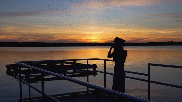Silhouette of graduate at sunset on the pier overlooking beautiful lake.