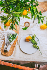Table setting with white plate, cutlery, linen napkin and orange tree branch decoration on white linen tablecloth . Close up. Table with table setting and shair