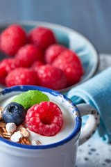 Yogurt with muesli, raspberry and nuts, healthy dessert on light blue background