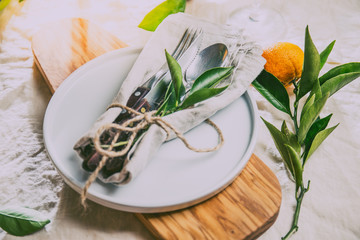 Table setting with white plate, cutlery, linen napkin and orange tree branch decoration on white linen tablecloth . Close up. Table with table setting and shair