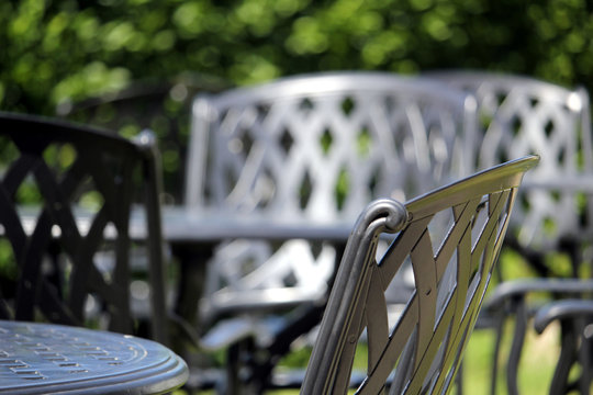 Close up of a wrought iron chair, with other similar chairs and tables in the out of focus background on a lovely sunny day
