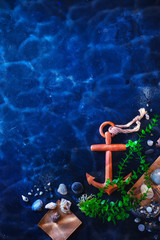 Anchor and seaweeds in an underwater still life on a dark background with water ripple. Sea travel and diving concept with copy space