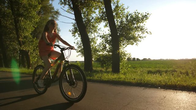 Front full length view of teen girl on a bike cycling through countryside and enjoying freedom during sunset. Positive peaceful shot of teenage girl. Sun flare through the trees. Steadicam shot