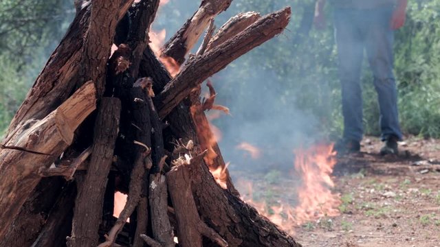 Man sets up a fire in the bush field. Stands and stare at it.