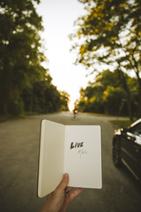 A notebook that says, "Live Mas," is held up by a man as the sun sets in the background.