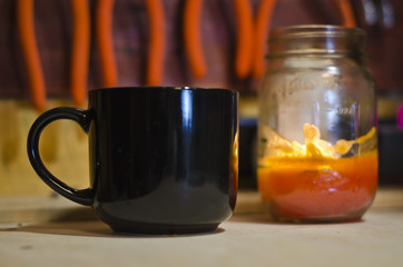 A blank black coffee mug and a candle in a mason jar on the shop work bench.