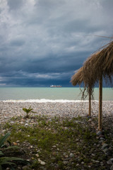 Beautiful beach view with dramatic sky of subtropical coastline in Batumi, Georgia Black Sea resort city with tourist shack made of straw.