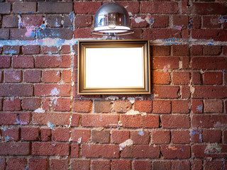 Mock up blank wooden picture frame hanging on grungy old red brick wall with spotlight above. Vintage style artwork, painting or picture background template in room.