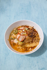 Thai style spicy Tom yum egg noodle with roasted pork soup on blue table background