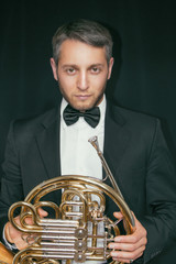 French horn player. Music instrument horn in the hands of hornist. A man in a suit and in a butterfly with a musical instrument. (Waldhorn)