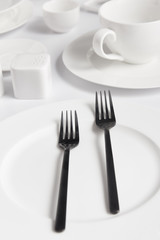 close up view of forks, various plates and saltcellar on white table