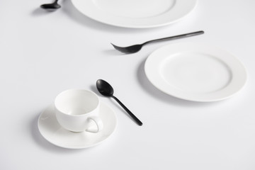 selective focus of cup, spoons, fork and various plates on white table