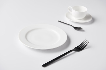 selective focus of plate, fork, spoon and cup on white table