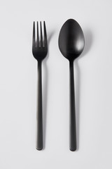 top view of black fork and spoon on white background, minimalistic concept