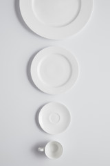 Top view of arranged various plates and cup in row on white table, minimalistic concept
