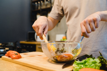 Happy beautiful asian man prepare salad food in the kitchen. Young asian male cooking healthy food while staying at home. Man lifestyle at home concept.