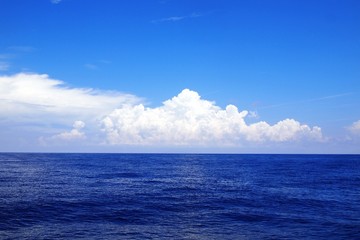 White puffy cumulus clouds with shades of blue over sea horizon  