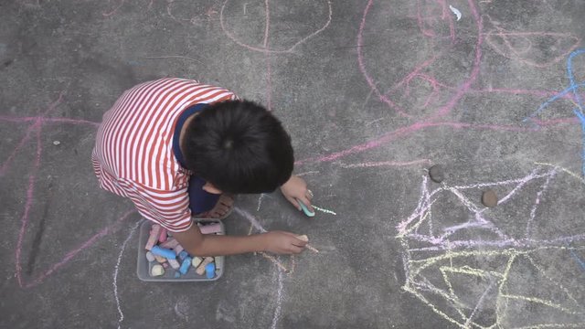 Little boy drawing and coloring by chalk on the ground