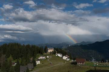 tiny alpine village and ski lift in the Swiss Alps with a great view of a rainbow and mountain...