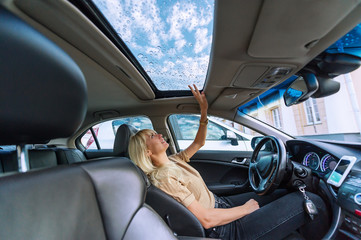 Blonde woman in modern car. Raindrops on a glass roof of the car
