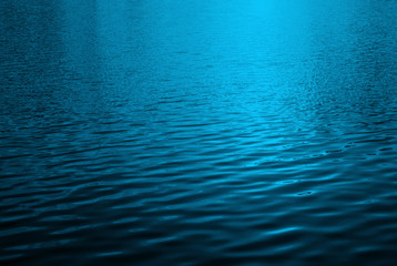 Blue water surface with bright sun light reflections, water in swimming pool background closeup