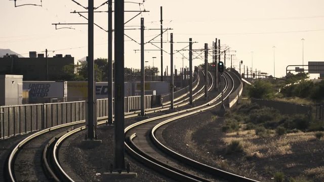 Light rail train travels down track towards sunset