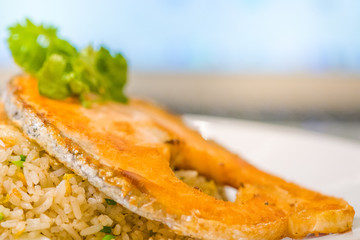 fried sliced salmon with fried rice.man hands use fork and spoon for fusion food.sliced salmon with rice on white plate in restaurant or cafe.man sitting and eating sliced salmon on laptop background
