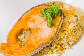 fried sliced salmon with fried rice.man hands use fork and spoon for fusion food.sliced salmon with rice on white plate in restaurant or cafe.man sitting and eating sliced salmon on laptop background