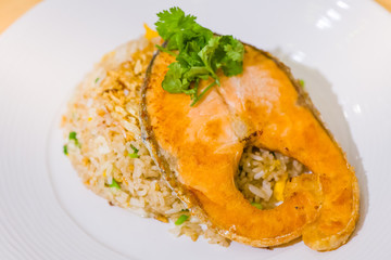 fried sliced salmon with fried rice.man hands use fork and spoon for fusion food.sliced salmon with rice on white plate in restaurant or cafe.man sitting and eating sliced salmon on laptop background