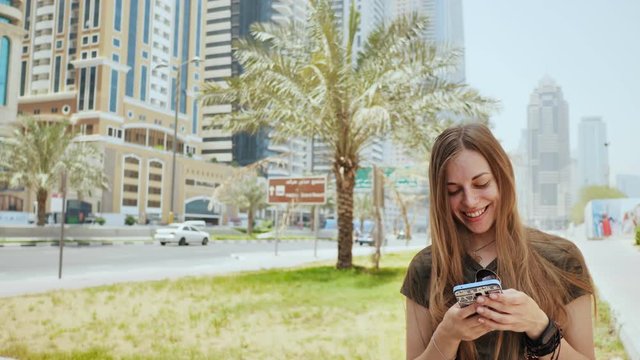 The girl dials a number or message on the smartphone against the backdrop of the city streets of Dubai.