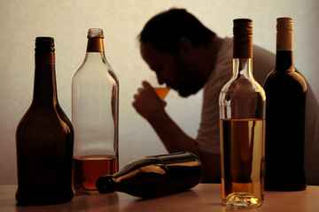 Fototapeta silhouette of anonymous alcoholic person drinking behind bottles of alcohol  obraz
