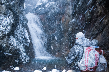 Two warmly dressed people near a waterfall in snow storm in Iceland