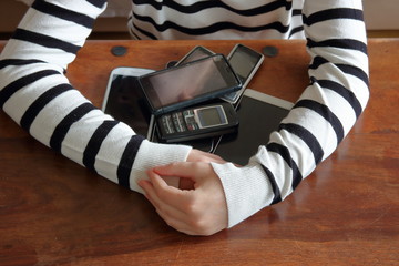 Ręce dziewczynki obejmują stos telefonów komórkowych, smartfonów leżących na drewnianym stole