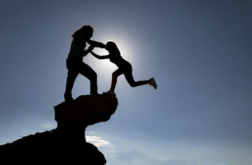 Young woman climbing rocks helped by her boyfriend