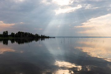 Perfectly symmetric and spectacular view of a lake, with clouds, sky and sun rays reflecting on water