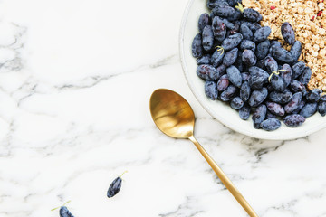 Fresh ripe honeysuckle berries and muesli in a ceramic bowl on a grey marble table. Healthy breakfast