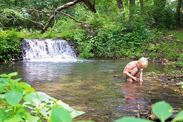Little Boy Exploring in Nature Looking for Rocks in the River