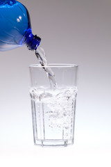 Blaue Flasche schenkt Wasserglas ein (Hochformat)